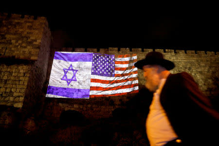 A man walks by as the Israeli national flag and an American one are projected on a part of the walls surrounding Jerusalem's Old City December 6, 2017. REUTERS/Ronen Zvulun