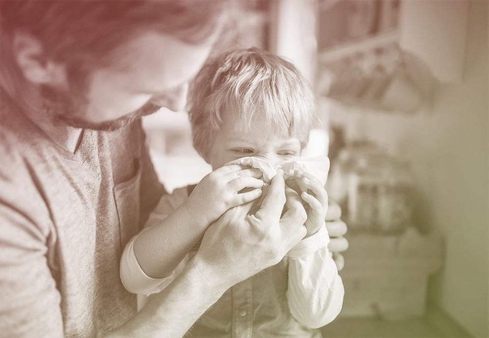 A father looking after son indoors, blowing his nose.