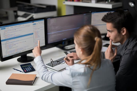 Two software engineers working together with multiple monitors displaying source code.