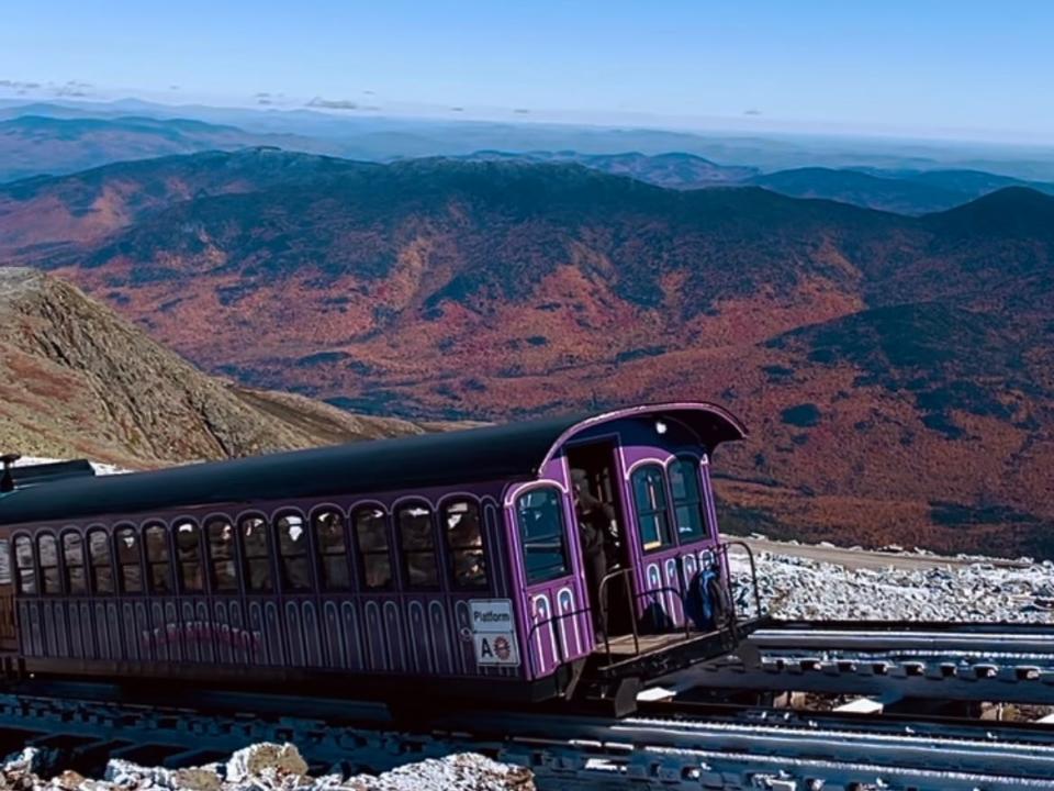 Purple train arrive at the summit of an icy mountain backdropped by valleys with orange trees