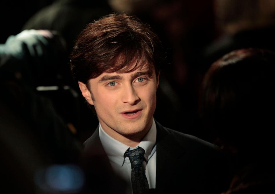 British actor Daniel Radcliffe arrives at a cinema in London's Leicester Square for the world premiere of Harry Potter and the Deathly Hallows Part 1, as masked actors stand behind them, Thursday, November 11, 2010. (AP Photo/Lefteris Petarakis)