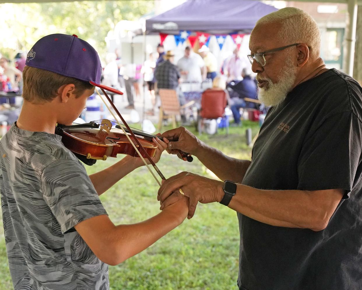 River Raisin Ragtime Revue music director emeritus William Hayes of Ypsilanti, right, shows Nick Baty, then 11, of Canton the violin July 9, 2022, in the "instrument petting zoo" at the Revue's Ragtime Extravaganza in Adrian.