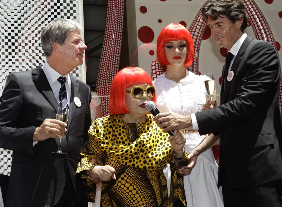 A model poses beside Japanese artist Yayoi Kusama, center, Louis Vuitton CEO Yves Carcelle, far left, and Vuitton second-in-command Jordi Konstans in front of the windows Kusama helped design at Vuitton's flagship Fifth Avenue store for the unveiling of a new collaborative collection by Kusama and Vuitton creative director Marc Jacobs in New York, Tuesday, July 10, 2012. (AP Photo/Kathy Willens)