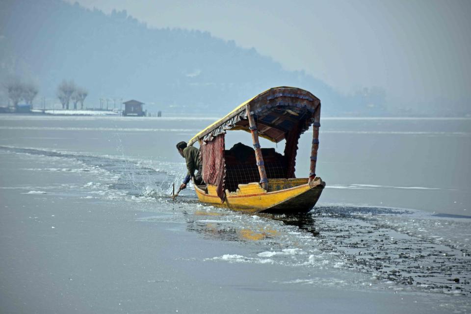 A local shikarawala trying to break the sheet of ice covering the Dal Lake in order to row across the lake.