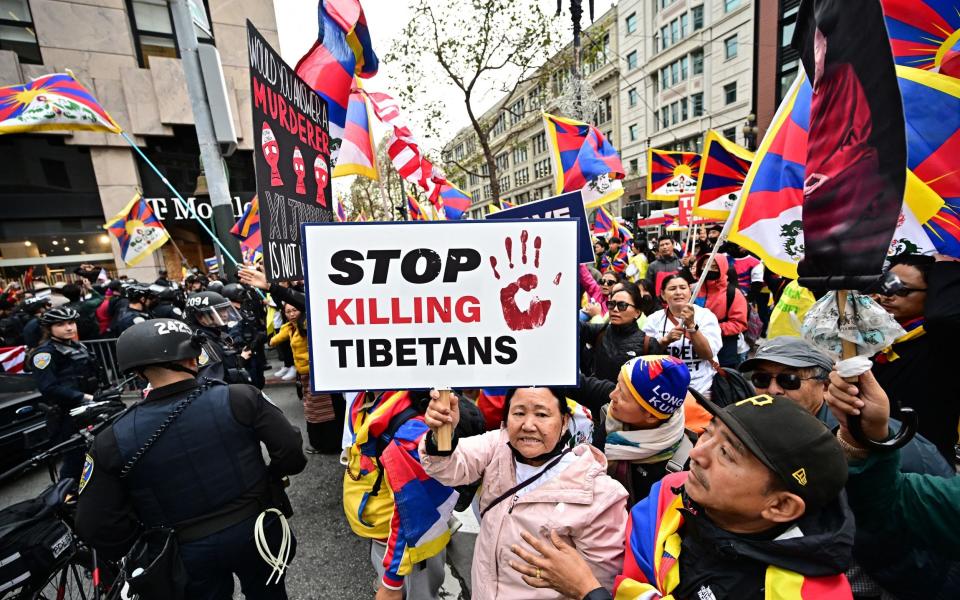 An older woman holds a sign which reads 'Stop Killing Tibetans' while police keep a crowd back