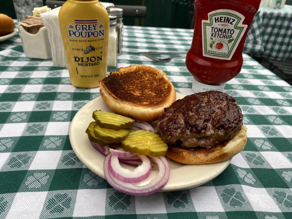 A hamburger on a plate with pickles and onions on the side.