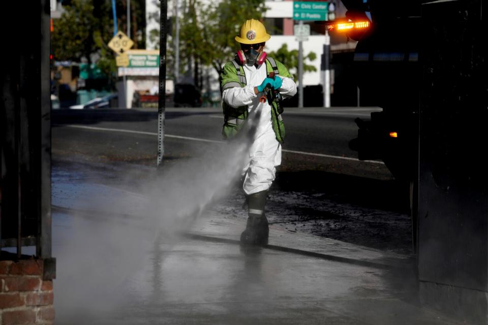 A worker in a helmet sprays water from a hose.