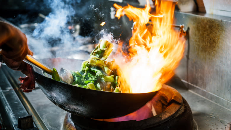 Close-up of a hand tossing a flaming wok
