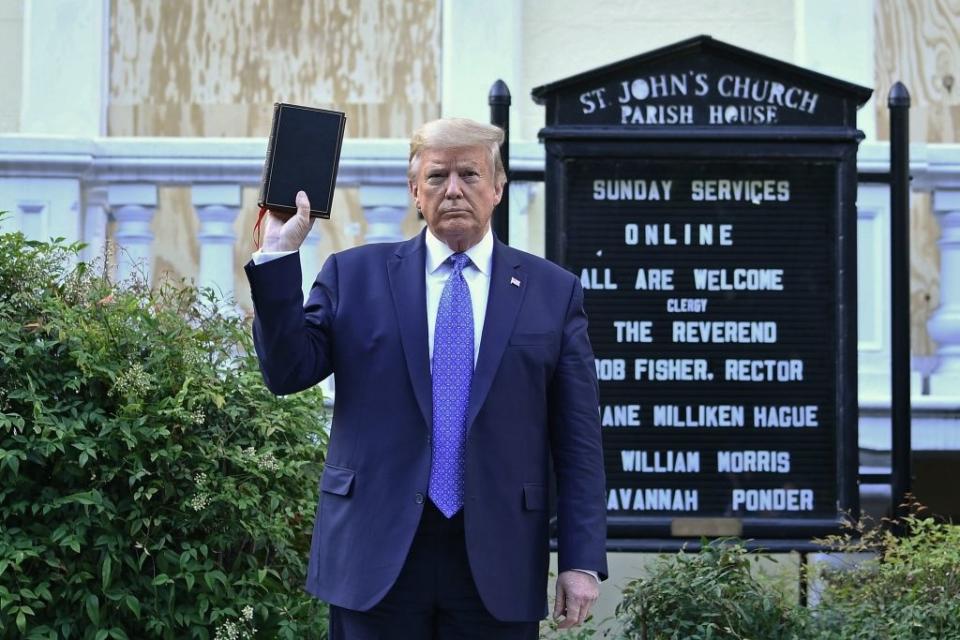 Donald Trump holds a Bible in front of St. John's Church Parish House; church signage in background displays Sunday Services Online information and clergy names