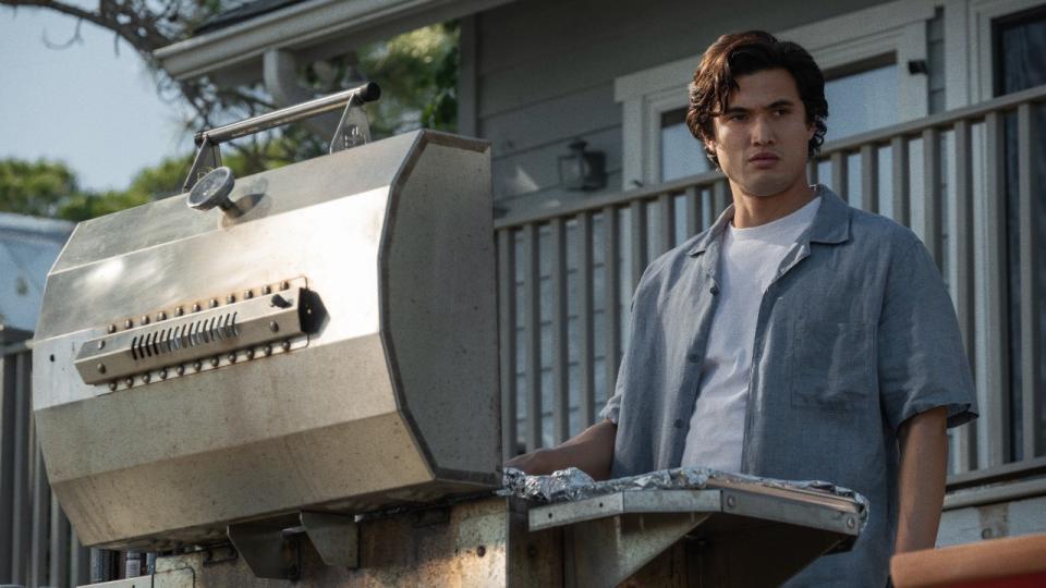 Charles Melton as Joe standing behind a BBQ.