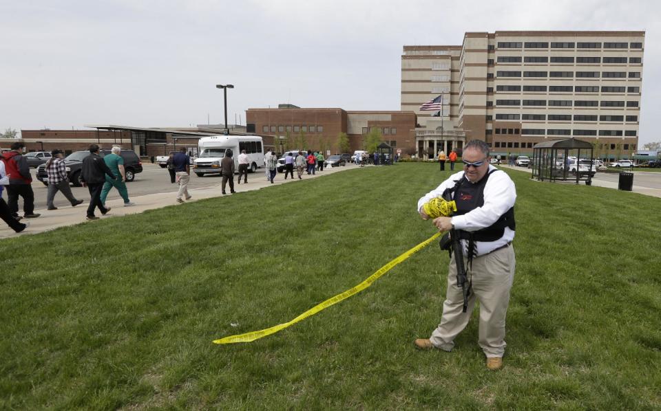 A police official takes down yellow police tape outside a Veterans Affairs hospital after telling people who were evacuated they could reenter the building, Monday, May 5, 2014, in Dayton, Ohio. A city official says a suspect is in police custody after a shooting at the Veterans Affairs hospital that left one person with a minor injury. (AP Photo/Al Behrman)