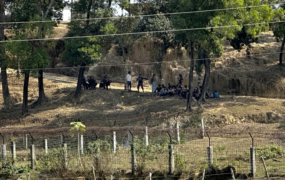 Members of Myanmar Border Guard Police, in civilian clothing, sit under the shade of trees after abandoning their posts following fighting between Myanmar security forces and Arakan Army, an ethnic minority army, as Bangladesh border guards stand guard in Ghumdhum, Bandarban, Bangladesh, on Monday, Feb. 5, 2024. Nearly a hundred members of Myanmar's Border Guard Police have fled their posts and taken shelter in Bangladesh during fighting between Myanmar security forces and an ethnic minority army, an official of Bangladesh's border agency said Monday. (AP Photo/Shafiqur Rahman)