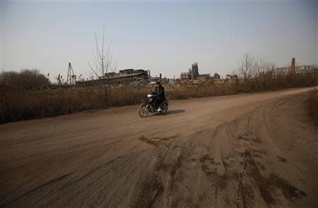 A man rides an electronic bicycle along a muddy road near an abandoned steel mill (back) of Qingquan Steel Group in Qianying township, Hebei province February 18, 2014. REUTERS/Petar Kujundzic