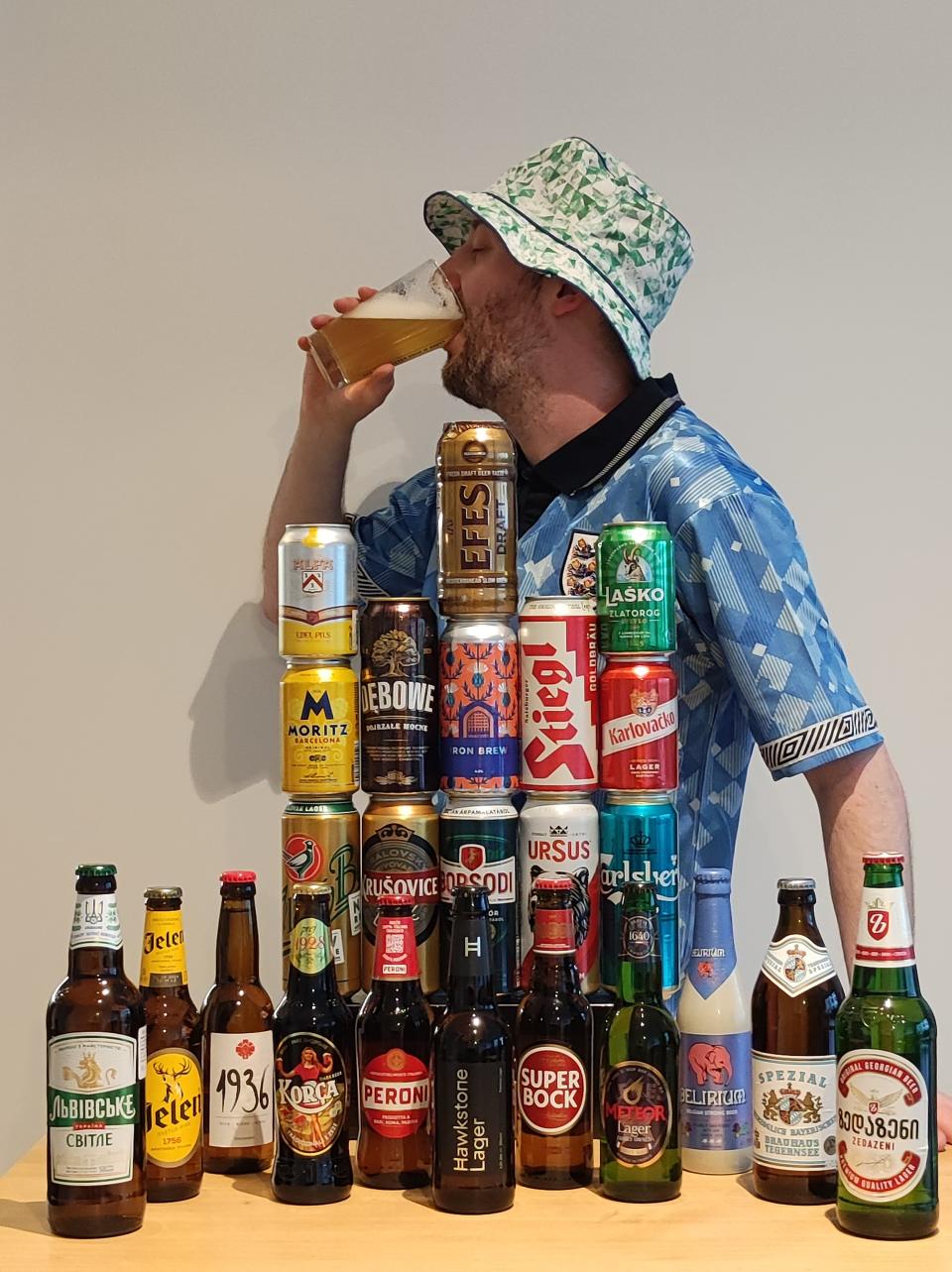 Gus Hully drinking a beer and standing in front of a table where the 24 beers are placed 