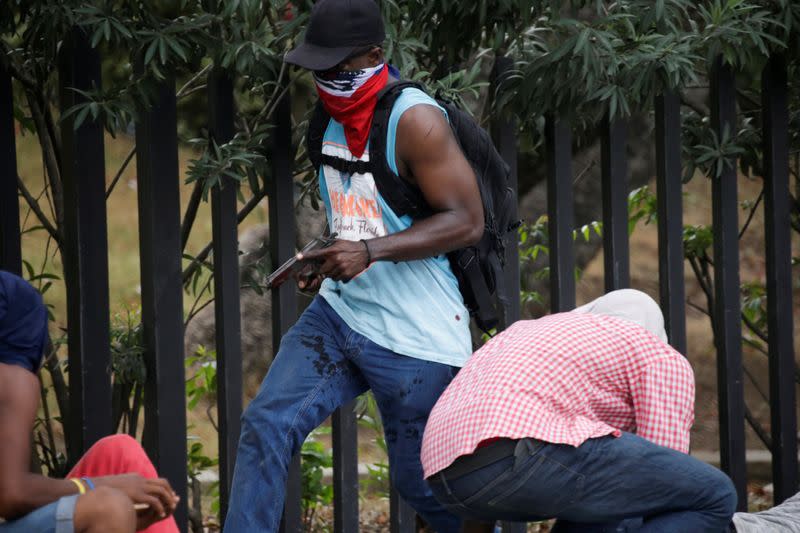 A masked protester carrying a gun runs for cover during a shooting in Champ de Mars, Port-au-Prince