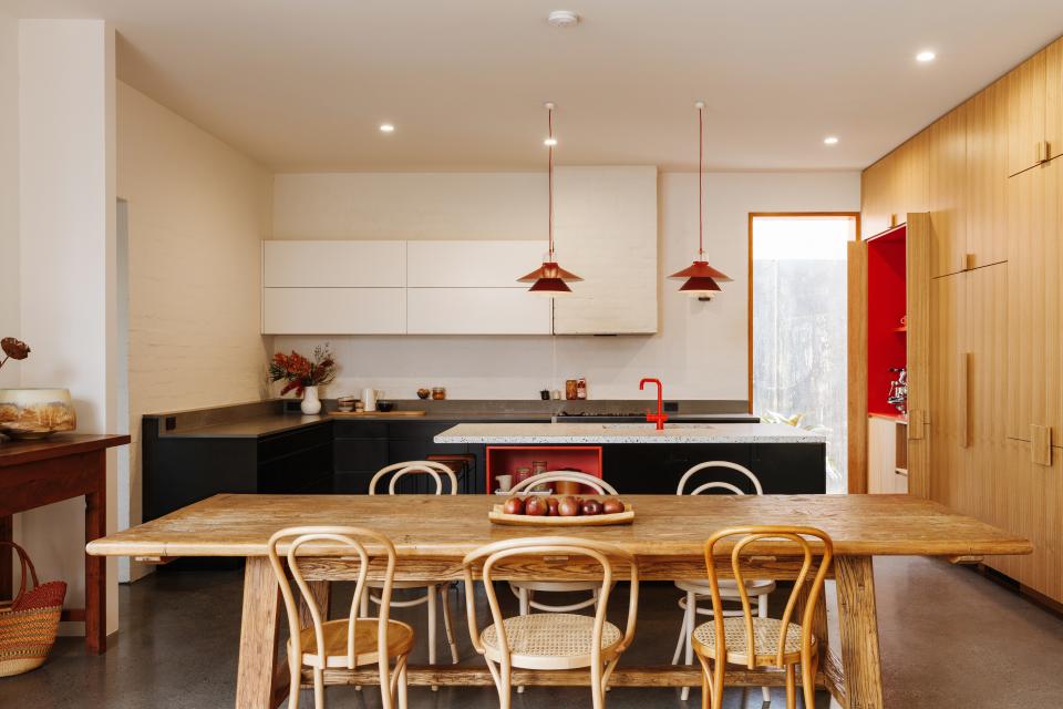“This kitchen needed to feel cohesive, since the living area is adjacent,” Kate says. A wood dining table and chairs further link the two spaces, which are also joined by painted white brick walls, wood accents, and pops of red.