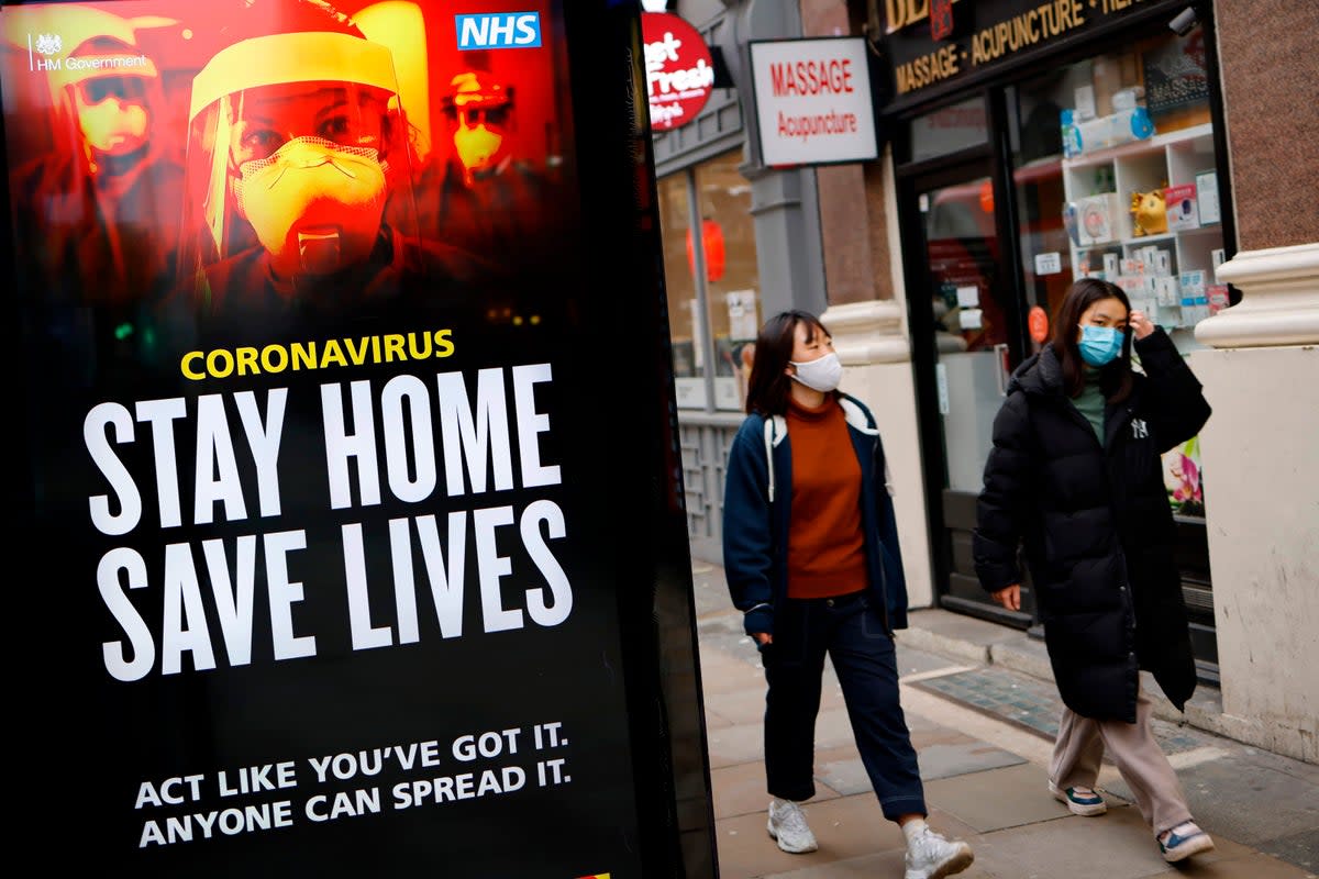 Pedestrians wearing facemasks walk past NHS signage promoting "Stay Home, Save Lives" on a bus shelter (AFP via Getty Images)