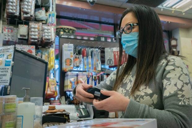 Lili Tran at the cash register inside Tap Phong Trading Co. The store plans to open Monday when some COVID-19 restrictions are lifted. (Sam Nar/CBC - image credit)
