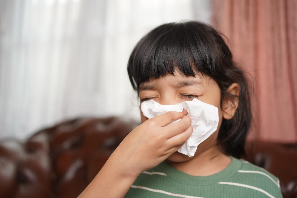 Asian kid girl sick with sneezing on nose and cold cough on tissue paper because of influenza and illness or virus bacteria.