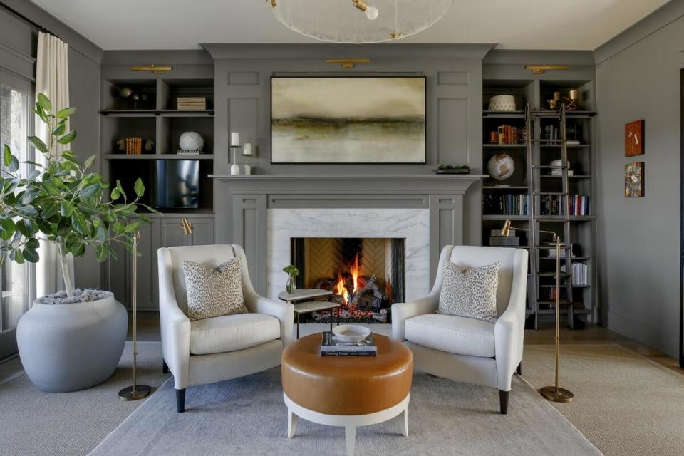 A cozy pair of seats in front of the fireplace each boasts its own reading lamp