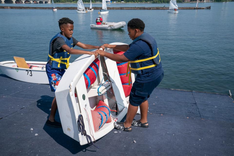 Dean Cole, 9, of Warren, left, works together with Challenge the Wind crewmate Austin De'Andre Shepard, 10, of Detroit, to flip over their Optimist (opti) sailboat to get it assembled for sailing on the Detroit River on Monday, July 24, 2023, from the banks of the Belle Isle Boat House. Challenge the Wind was started by the Detroit Community Sailing Center, which teaches youths ages 10-17 how to sail. The emphasis is on water safety and STEM to help increase access to Detroit's waterways for youths who would otherwise not get the opportunity.