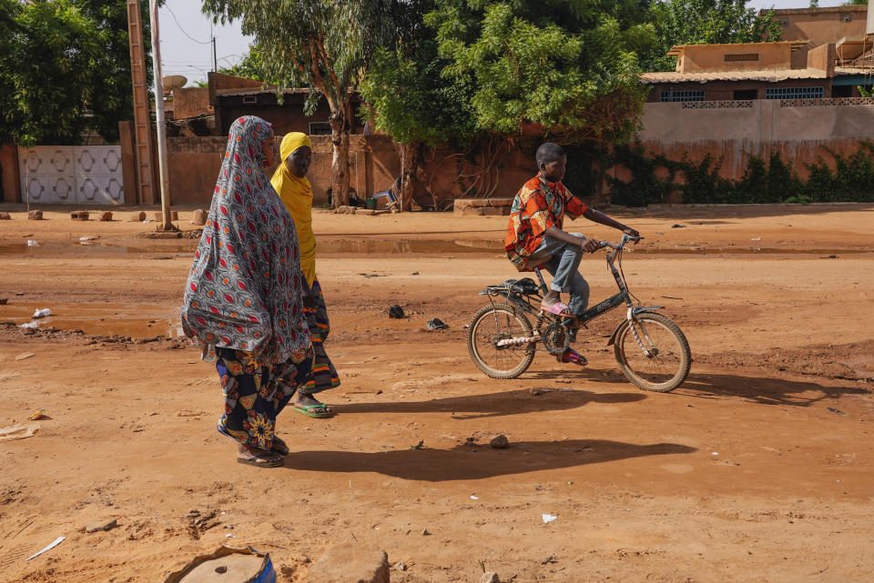 Two women walk as a boy cycles in the streets of Niamey, Niger, Sunday, Aug. 13, 2023. People marched, biked and drove through downtown Niamey, chanting "down with France" and expressing anger at ECOWAS. (AP Photo/Sam Mednick)