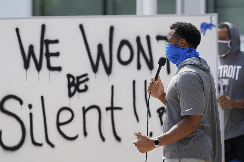 Trey Flowers, wearing a face covering, speaks into a microphone in front of a whiteboard that reads, "We won't be silent!"