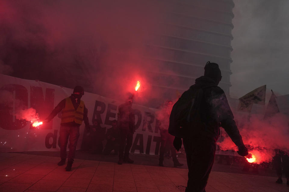 Demonstrators holding flares protest against the pension reforms outside the Euronext Paris building at La Defense business district in Paris, Thursday, April 20, 2023. Union activists stage scattered actions to press France's government to scrap the new law raising the retirement age. (AP Photo/Thibault Camus)