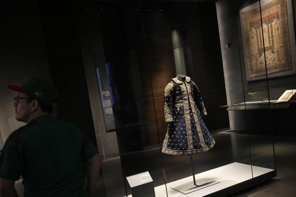 A visitor stands near a coat from India at the Museum of Islamic Art in Doha, Qatar, Tuesday, Nov. 22, 2022. For many of the visitors descending on Qatar for The World Cup, Doha's Museum of Islamic Art provides a peek into diverse aspects of Muslim heritage, art and craftmanship. The collection at MIA, as the museum is known, spans three continents and many centuries. (AP Photo/Christophe Ena)