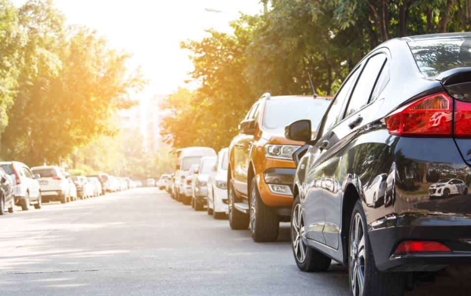 A black car is parked against the flow of traffic in an Australian street. 