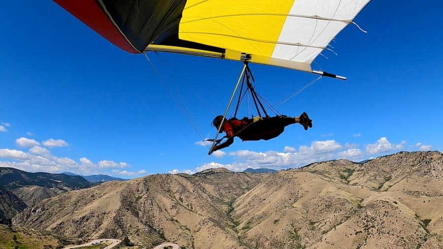 A man high above the mountain foothills of Colorado's Rocky Mountain front range with a red, black, yellow and white hang glider