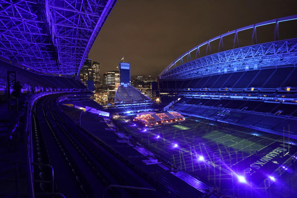 Colored lights glow as night falls while people eat dinner in an outdoor dining tent set up at Lumen Field, the home of the Seattle Seahawks NFL football team, Thursday, Feb. 18, 2021, in Seattle. The "Field To Table" event was the first night of several weeks of dates that offer four-course meals cooked by local chefs and served on the field at tables socially distanced as a precaution against the COVID-19 pandemic, which has severely limited options for dining out at restaurants in the area. (AP Photo/Ted S. Warren)