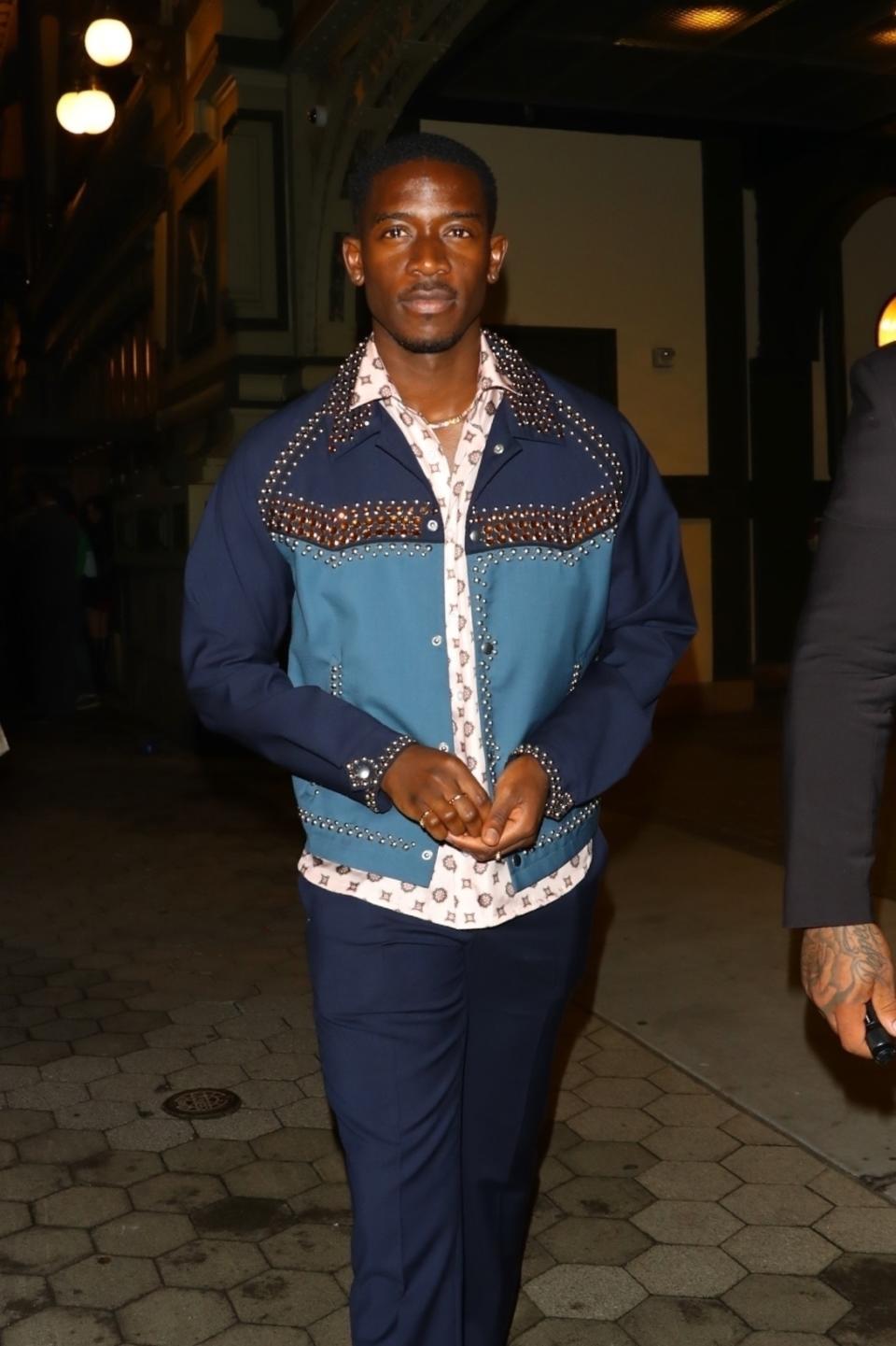 Mamoudou Athie in a studded collar shirt and matching pants on a walkway