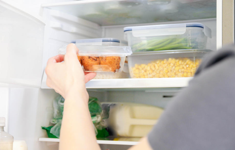 A person placing a container of food into a refrigerator, with various other containers and items visible inside