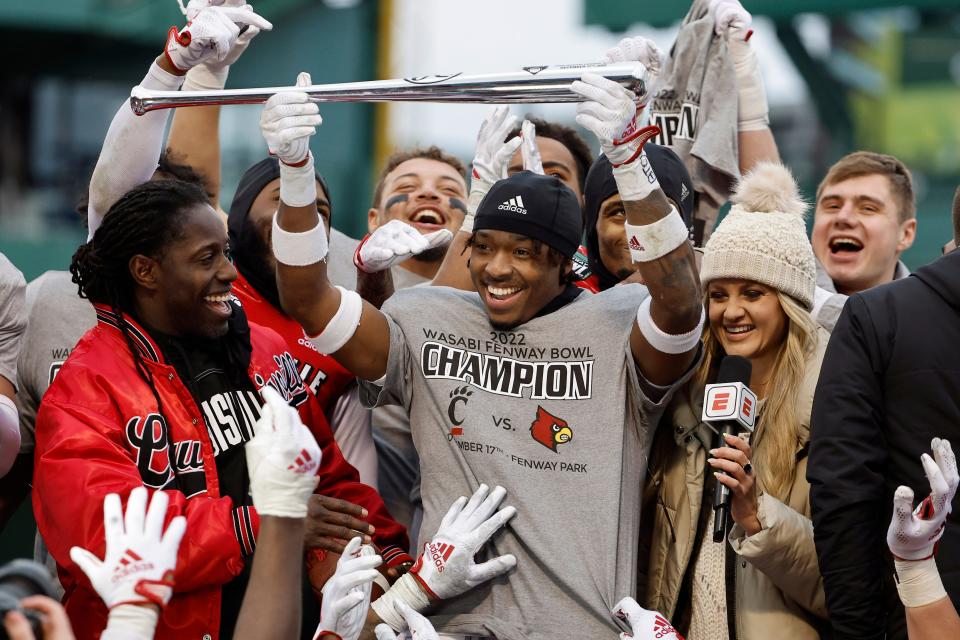 Louisville head coach Deion Branch, left, looks on as Jawhar Jordan holds up a silver baseball bat after being named the offensive MVP after their 24-7 win over Cincinnati in the Fenway Bowl NCAA college football game at Fenway Park, Saturday, Dec. 17, 2022, in Boston. (AP Photo/Winslow Townson)