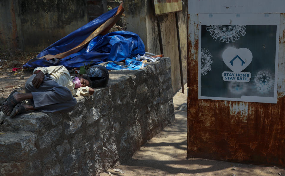 An Indian man sleeps next to a signage urging people to stay at home as a precaution against coronavirus in the premises of a hospital in Hyderabad, India, Thursday, April 29, 2021.(AP Photo/Mahesh Kumar A.)