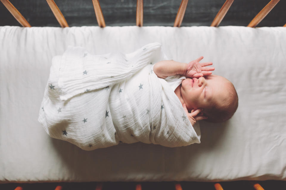 Swaddled newborn lies comfortably with eyes closed and a hand near the face