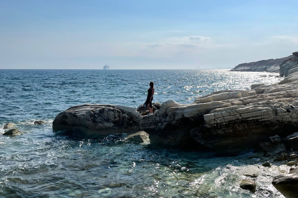 Photo of Elena, a young Russian who fled her country, standing on a rock on a beach.