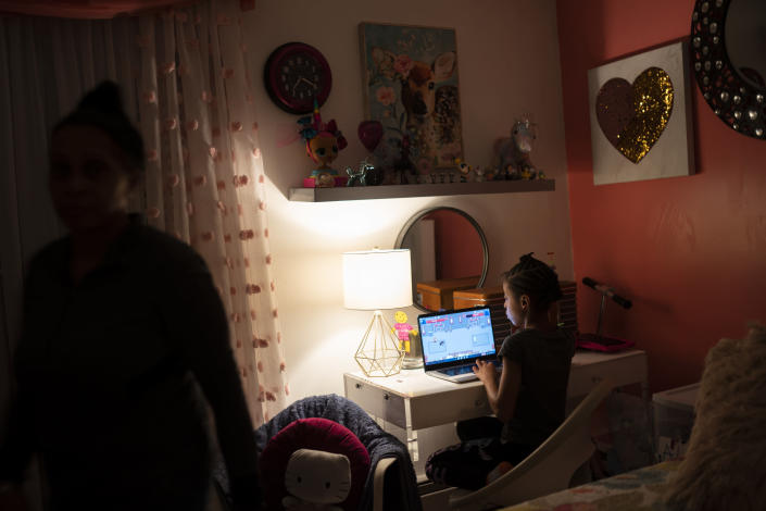 Abigail Schneider, 8, completes a level of her learning game on a laptop in her bedroom as her mother April steps toward the doorway, Wednesday, Dec. 8, 2021, in the Brooklyn borough of New York. As more families pivot back to remote learning for quarantines and school closures, reliable, consistent access to devices and home internet remains elusive for many students who need them to keep up with their schoolwork. (AP Photo/John Minchillo)
