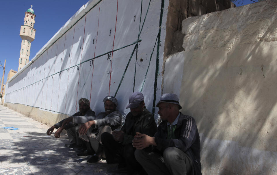 Men sit by a wall where electoral posters for the upcoming parliamentary elections will be placed, Thursday, May 20, 2021 in Ain Ouessara, 200 kilometres (125 miles) south of Algiers. Initially planned for April 22, the the legislative election will take place on June 12, 2021 in the North African country. (AP Photo/Fateh Guidoum)