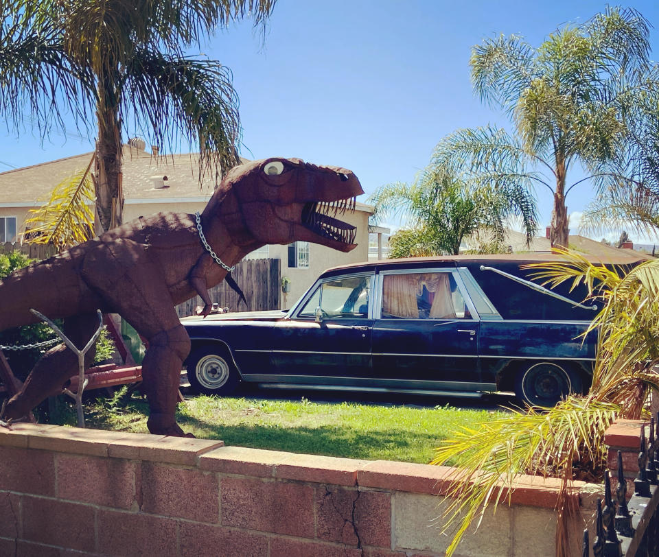 Louise’s dinosaur in her front garden with their prized hearse (Collect/PA Real Life)