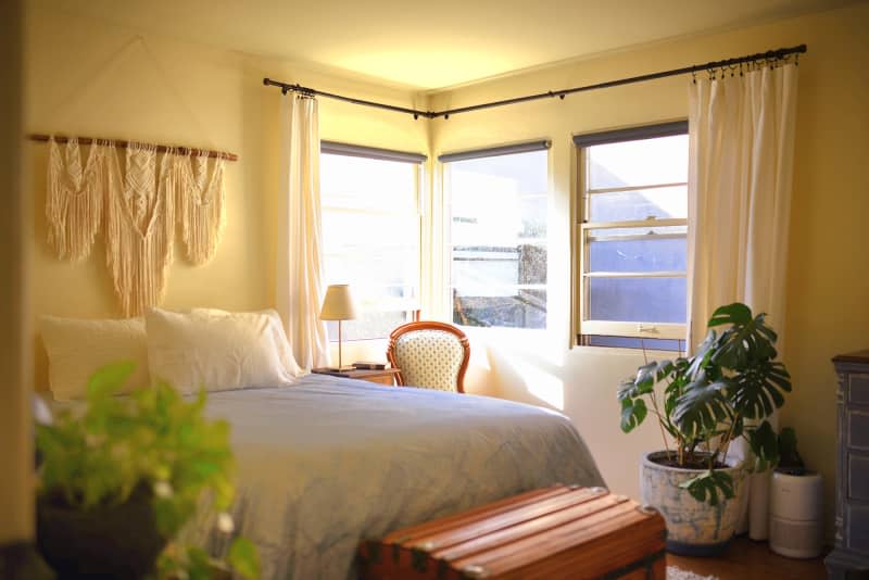 yellow bedroom with pale linens, textile art, and plants