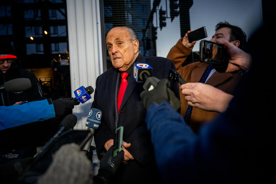 Rudy Giuliani speaks to reporters and microphones outside a building, while another man films him