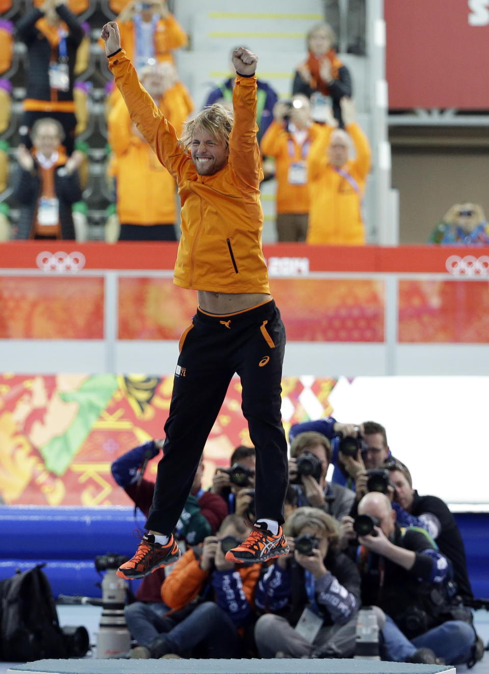 Photographers huddle in the background taking pictures of gold medallist Michel Mulder from the Netherlands as he jumps in celebration during the flower ceremony for the men's 500-meter speedskating race at the Adler Arena Skating Center at the 2014 Winter Olympics, Monday, Feb. 10, 2014, in Sochi, Russia. (AP Photo/David J. Phillip)