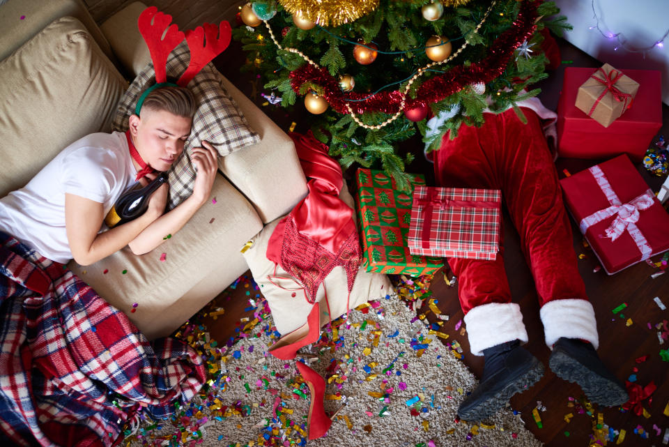 Young man sleeping on the sofa, while drunk Santa Claus sleeping under Christmas tree