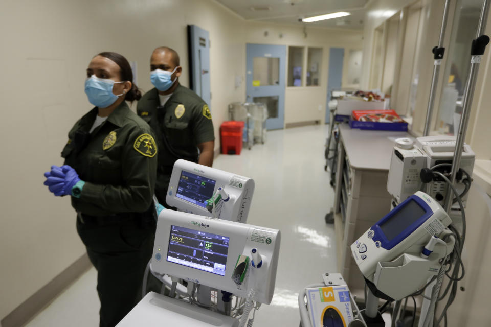 In this April 16, 2020, photo Christopher Lumpkin, right, and Sonia Munoz, custody assistants, walk in the hallway of the hospital ward at the Twin Towers jail in Los Angeles. Across the country first responders who've fallen ill from COVID-19, recovered have begun the harrowing experience of returning to jobs that put them back on the front lines of America's fight against the novel coronavirus. (AP Photo/Chris Carlson)