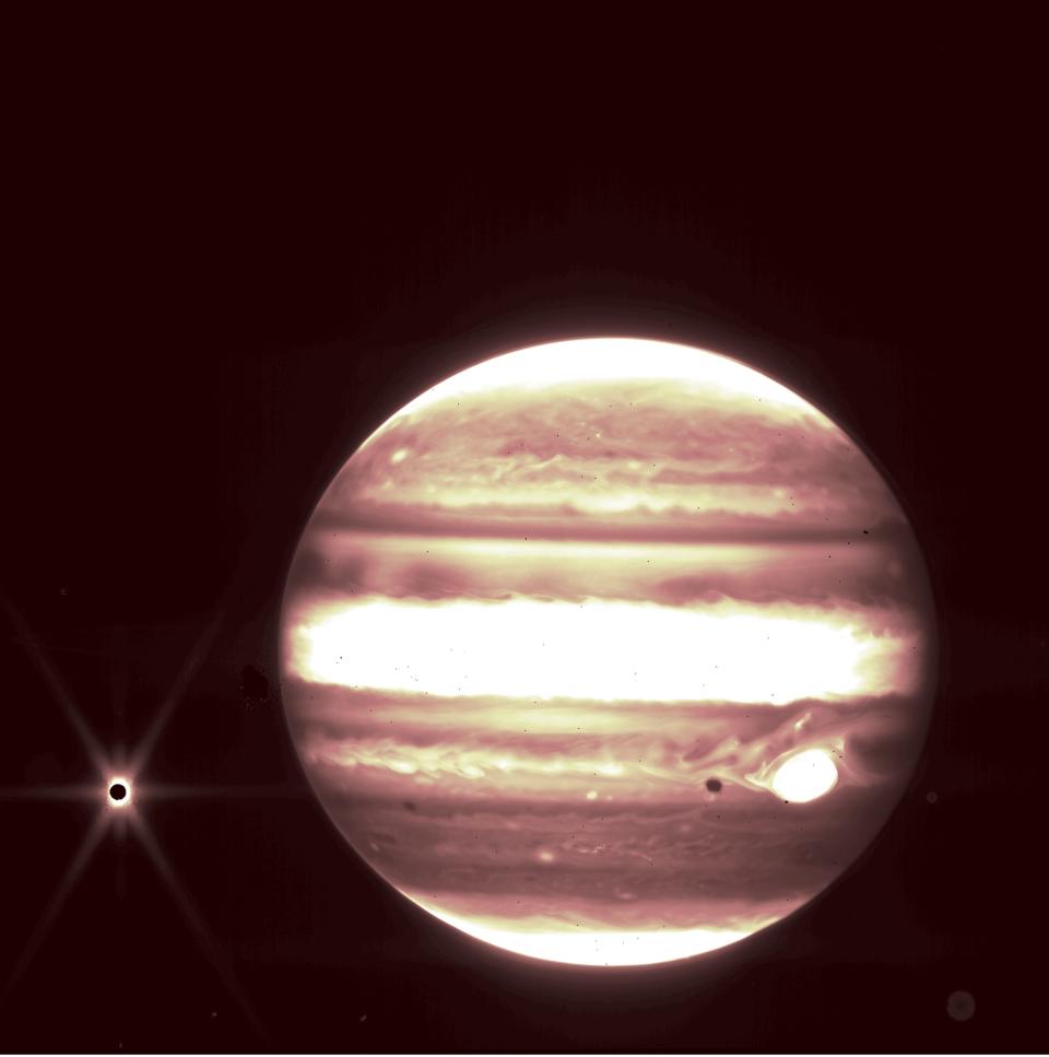 jupiter in white and orange infrared with dark moon europa surrounded by yellow light