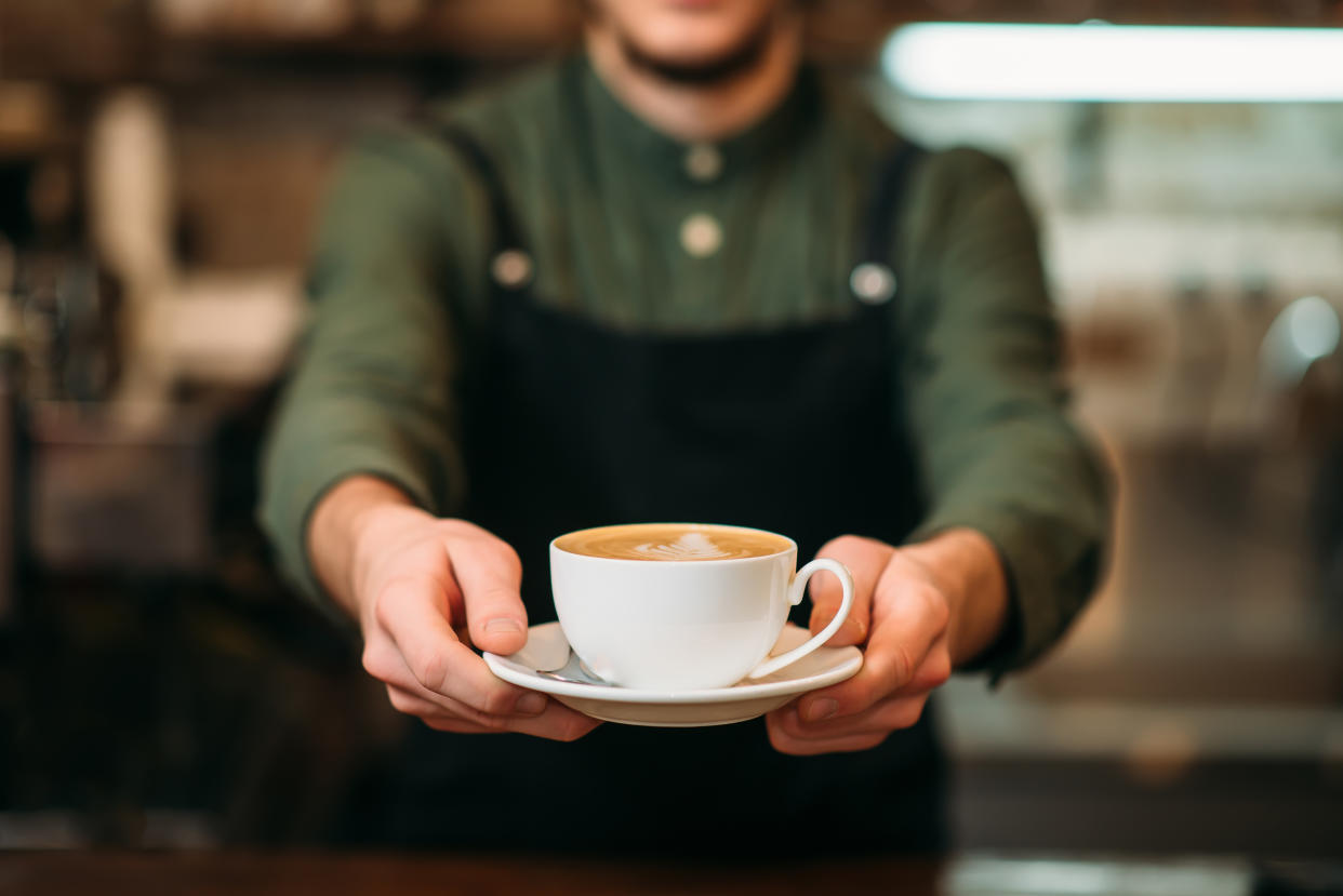 Waiter holding a cup of coffee with cream.