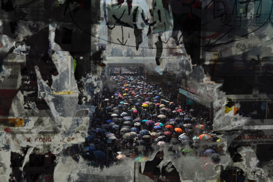 Marching anti-government protesters are seen through a window with peeled off posters in Hong Kong on Oct. 1, 2019. (AP Photo/Vincent Yu)