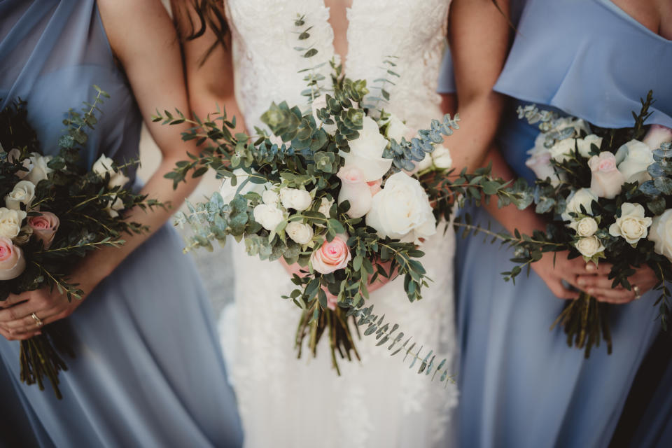 Bride in a lace dress and bridesmaids in blue, holding bouquets, at a wedding